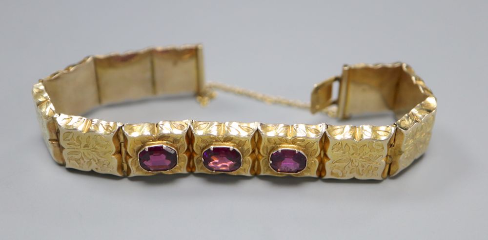 A Victorian engraved yellow metal and three stone garnet set hinged panel bracelet, with safety chain, gross 21.7 grams.